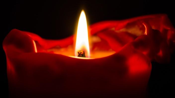 A single red candle burns against a dark background
